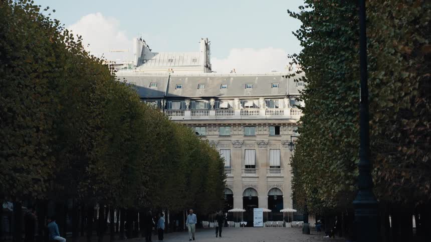 A stately Parisian building framed by a tree-lined walkway in a city park