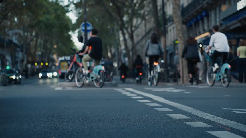 A slow-motion, out-of-focus view of cyclists and traffic navigating a European city street at dusk, seen from a low angle
