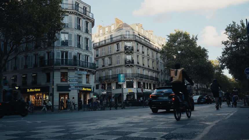 Slow motion captures the diverse flow of traffic, including cars, bicycles, and scooters, at a classic Parisian street intersection