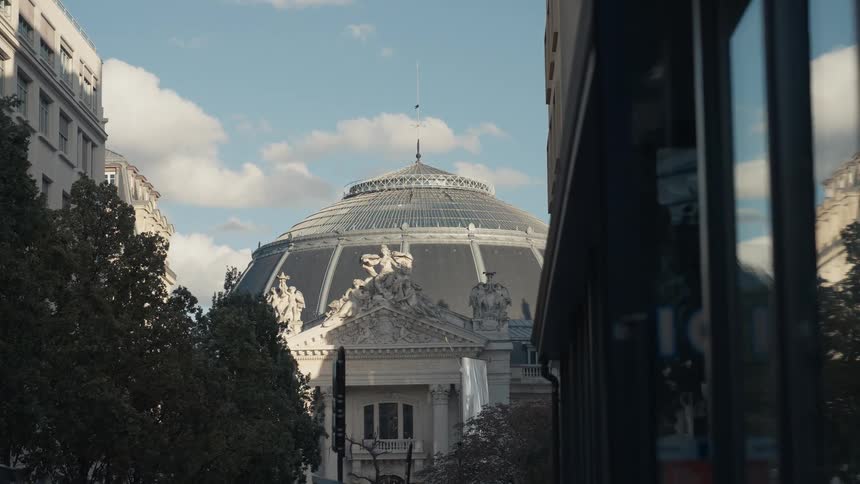 Sunlight illuminates the ornate dome of the Bourse de Commerce, viewed from a classic Parisian street