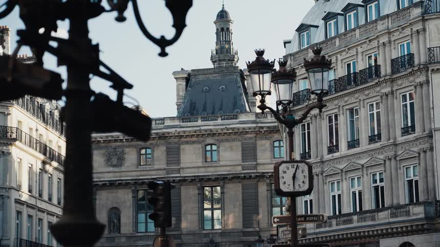 Ornate Parisian architecture stands timelessly behind a vintage street clock and changing traffic light