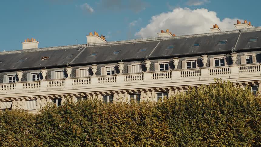 Sunlight illuminates the ornate facade of a traditional Parisian building behind a row of autumn trees