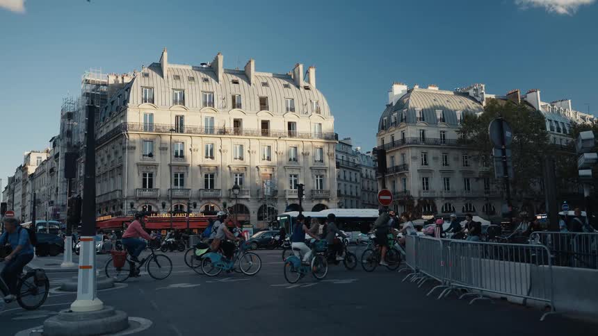 A slow-motion shot of a bustling intersection in Paris, where a crowd of cyclists navigates the street on a sunny day