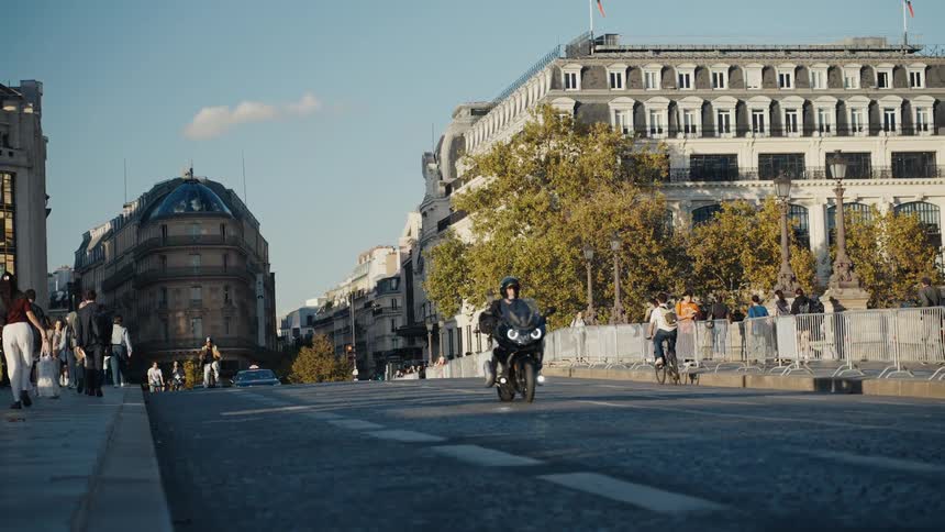 A motorcyclist rides towards the camera in slow motion on a cobblestone street in Paris with pedestrians and classic architecture in the background