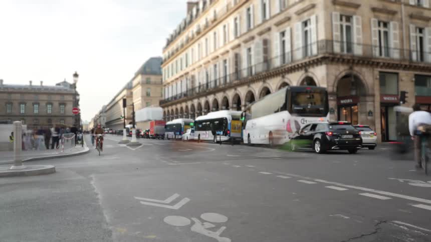 Time-lapse captures the bustling energy of a Paris street corner with blurred traffic, cyclists, and pedestrians moving through the city