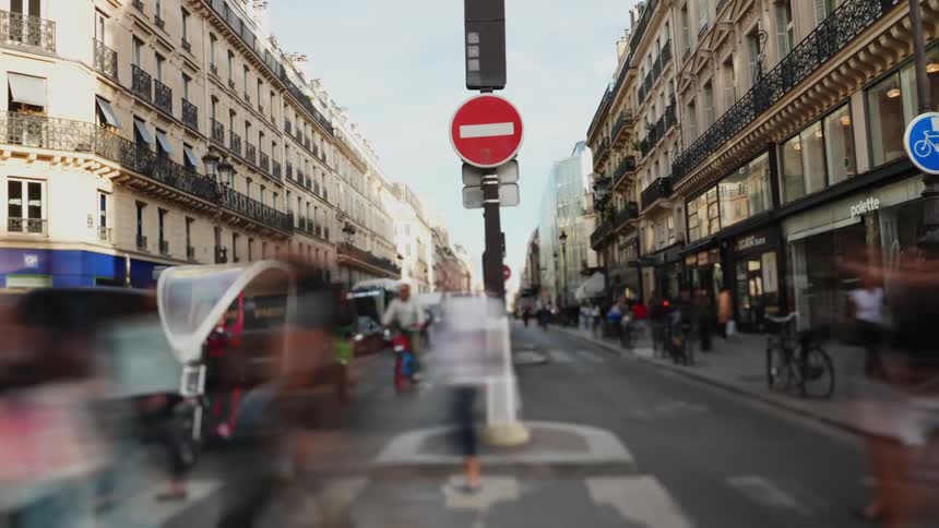 A dynamic time-lapse of a bustling Paris street, with blurred motion of pedestrians, cyclists, and traffic flowing through the city