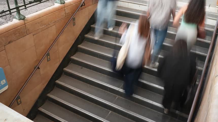 A high-angle time-lapse shows a blur of anonymous people rushing up and down the stairs of an underground station