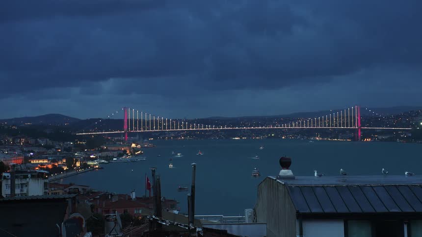 A dramatic timelapse captures the transition from dusk to night over the Bosphorus Bridge in Istanbul, as city lights illuminate and boats cross the water