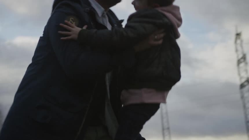 Joyful son runs in slow motion into his father's loving embrace in a rural field under a cloudy sky