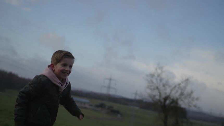 Slow motion shot of a happy brother and sister laughing and chasing each other through a rural field on an overcast day