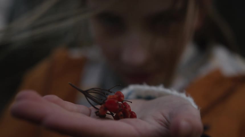 A curious young girl with windblown hair closely examines a small sprig of red berries in her palm