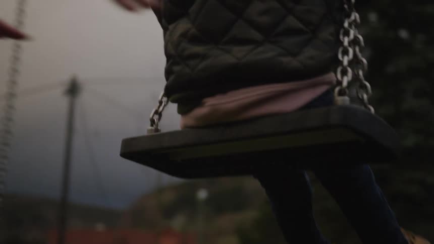 A mother gently pushes her young child on a swing at the park in slow motion