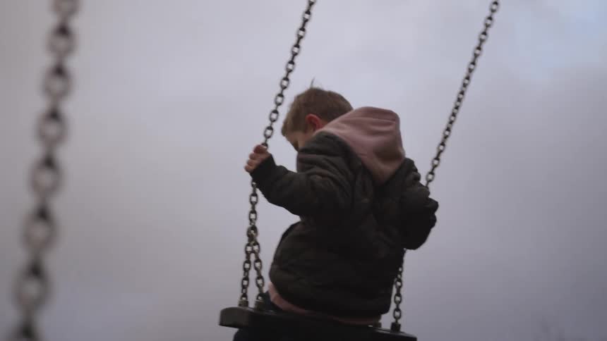Slow motion shot of a mother pushing her son on a swing set at the playground on a cloudy day