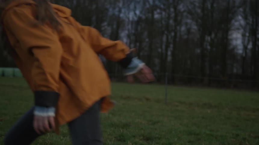 A happy brother and sister playfully chase each other through a rural meadow at dusk in slow motion