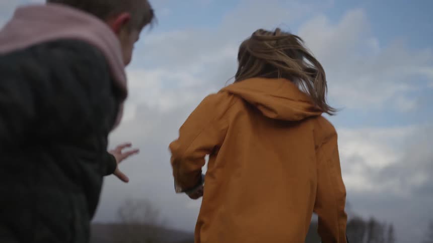 A young boy playfully chases his laughing friend through an open field in slow motion
