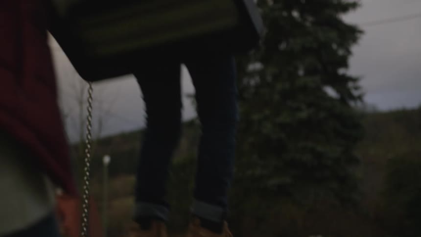 A mother gently pushes her young son on a swing in a park on an overcast day, filmed from behind in slow motion