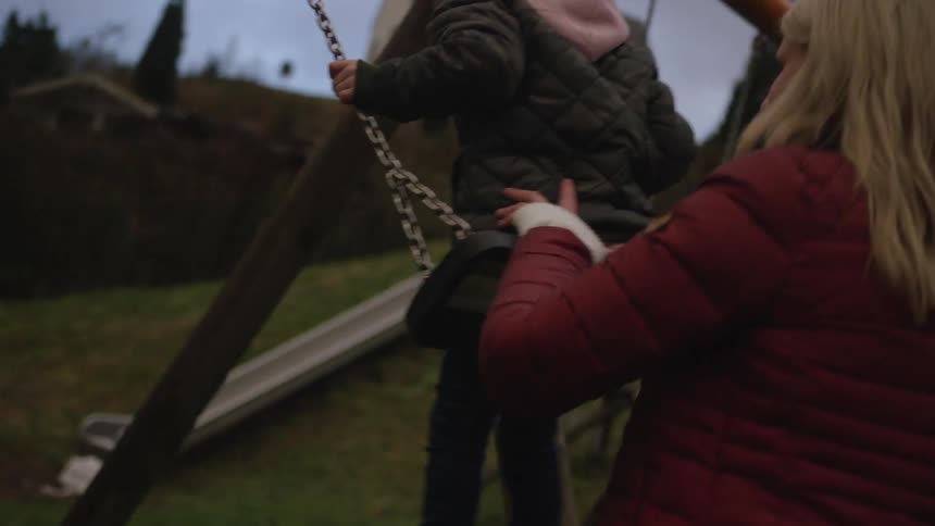 Slow motion shot of a mother pushing her smiling son on a backyard swing under a cloudy sky
