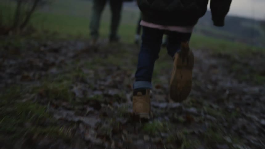 Low-angle slow-motion shot of a person's boots running through a muddy field covered in autumn leaves