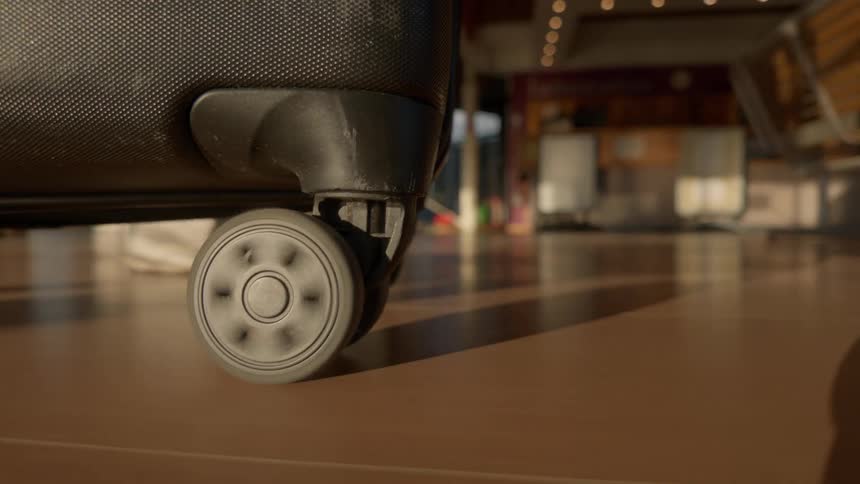 Low angle close-up of a rolling suitcase wheel as a traveler walks through an airport terminal