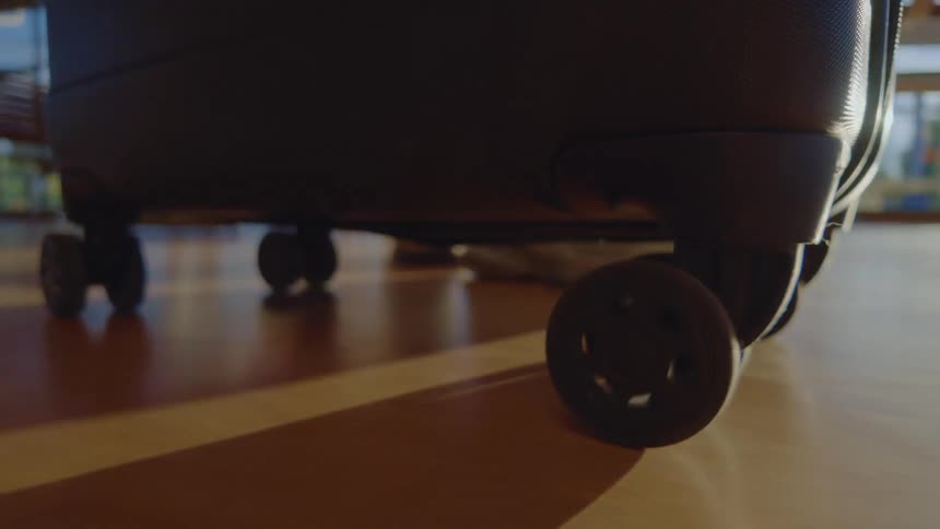 A close-up of a travel suitcase wheels resting on a polished floor as light and shadows pass by