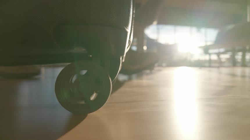 Close-up shot of a rolling suitcase wheel gliding across the floor of a sun-drenched airport terminal