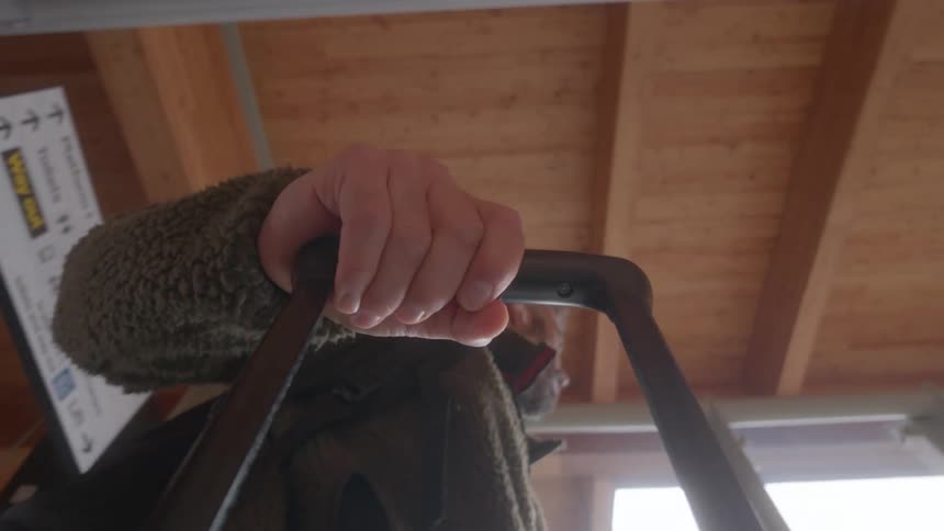 A low-angle point-of-view shot of a man pulling a rolling suitcase through a modern terminal with a wooden ceiling