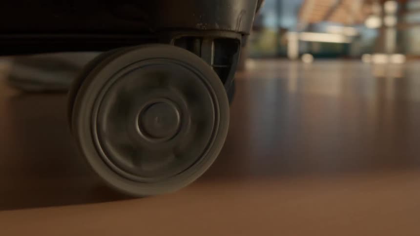 A close-up, low-angle shot of a suitcase wheel spinning as it rolls across the shiny floor of an airport terminal