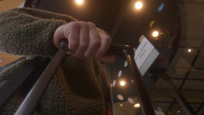 A unique low-angle shot from a suitcase captures a man walking through a revolving glass door into a modern, well-lit building