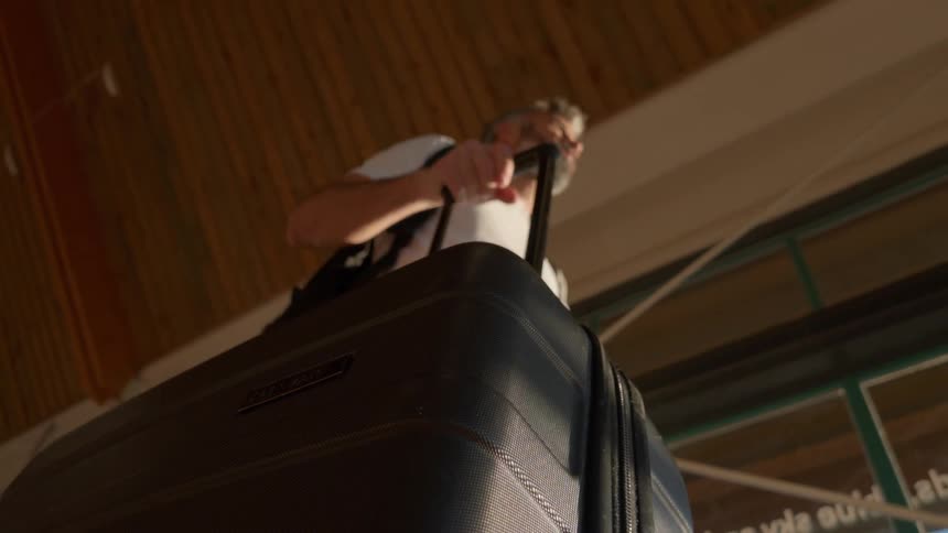 A low-angle slow-motion shot of a man pulling his suitcase as he walks through a terminal