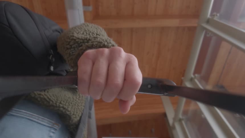 A first-person view from a luggage cart shows a traveler's hand gripping the handle while moving through a station