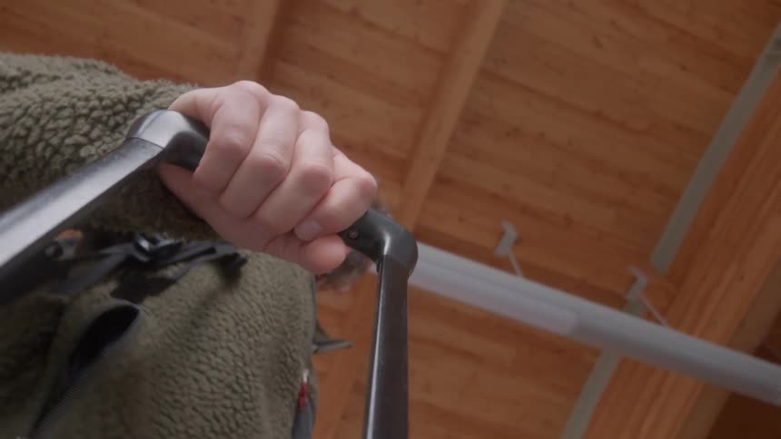 A low-angle close-up of a man's hand holding the handle of his rolling luggage while walking through a terminal