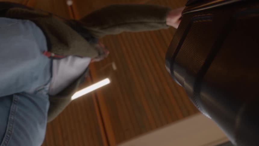 A man pulls his wheeled suitcase, shot from an out-of-focus low-angle perspective from the luggage