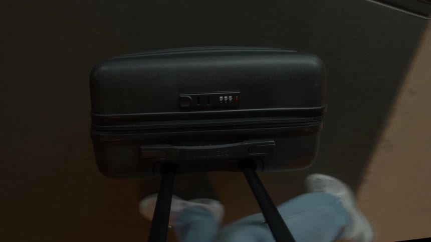 A top-down point-of-view shot of a person walking and pulling a black rolling suitcase