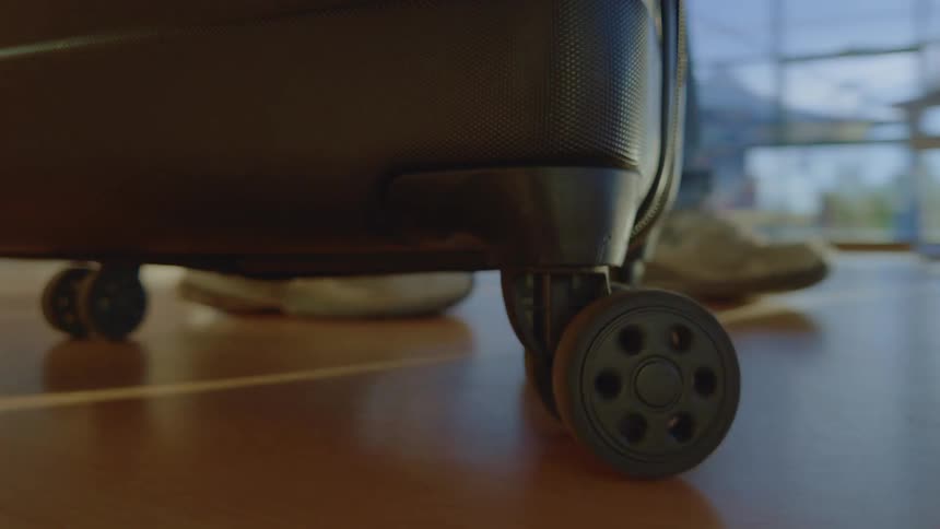 Low-angle close-up of suitcase wheels rolling across a polished airport floor as a traveler departs