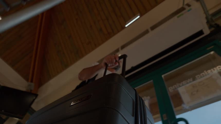 Low-angle slow-motion shot of a man pulling his rolling suitcase through a transit terminal