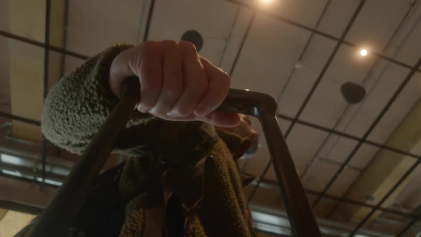 A traveler's hand grips a rolling suitcase handle as they walk through a modern building, filmed in a slow-motion low-angle shot
