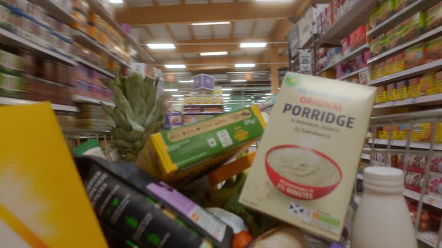 Point-of-view shot from inside a shopping cart as it is pushed through the aisles of a supermarket, with items being added