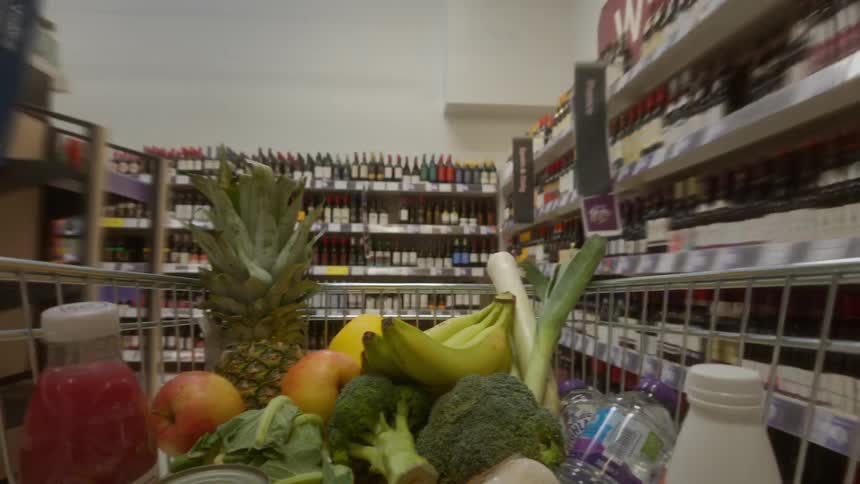 A time-lapse point-of-view from inside a shopping cart full of fresh groceries as it moves quickly through the aisles of a supermarket