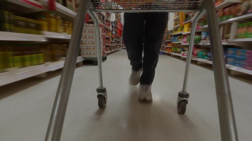 A low-angle point-of-view from underneath a shopping cart as a person pushes it down a supermarket aisle