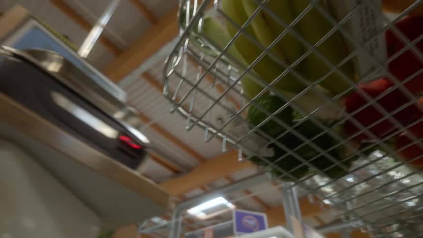 A low-angle point-of-view shot from a shopping basket full of fresh produce moving through a supermarket aisle