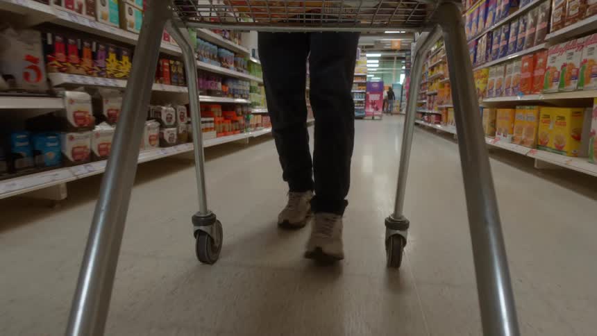 A low-angle point-of-view shot from a shopping trolley as a person pushes it down a brightly lit supermarket aisle
