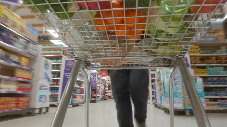A unique low-angle perspective from underneath a shopping cart full of groceries as it moves through the aisles of a supermarket