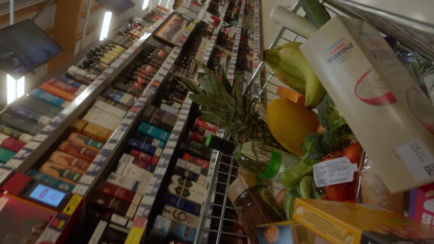 Unique canted angle point-of-view shot from a shopping cart full of groceries being pushed through the wine and spirits aisle of a large supermarket