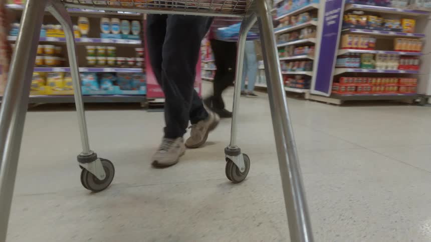 A low-angle point-of-view shot from a shopping cart as a person pushes it down the aisle of a grocery store