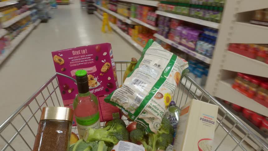 First-person perspective of a shopping cart full of groceries being pushed through the aisles of a supermarket