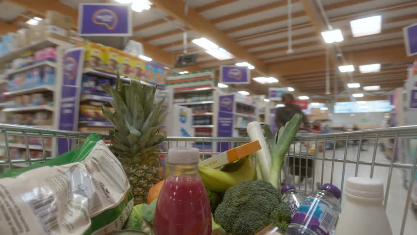 Point-of-view from a shopping cart full of fresh produce and groceries being pushed through a supermarket