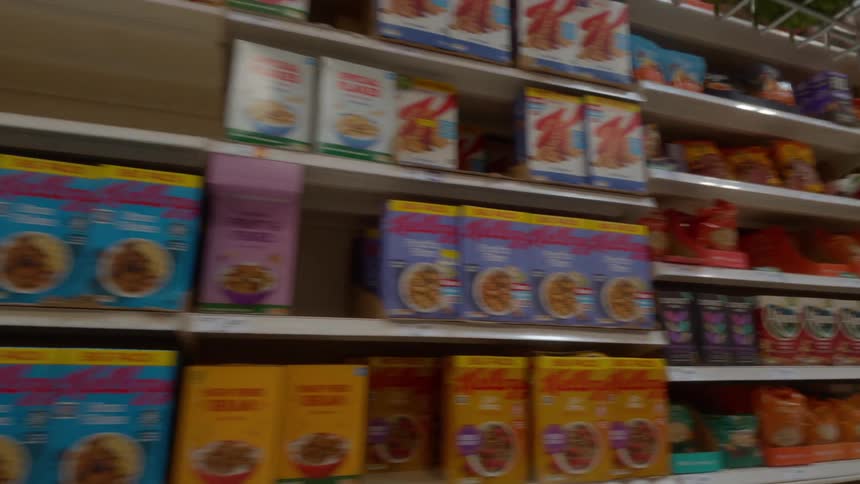 A blurry, low-angle point-of-view shot tracks slowly through the coffee and cereal aisles of a grocery store