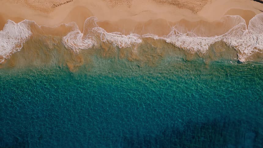 A serene and calming top-down aerial view of turquoise ocean waves gently washing ashore on a golden sand beach