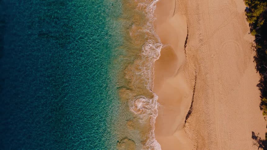 Calm aerial top-down vertical view of turquoise waves washing over a pristine sandy shore