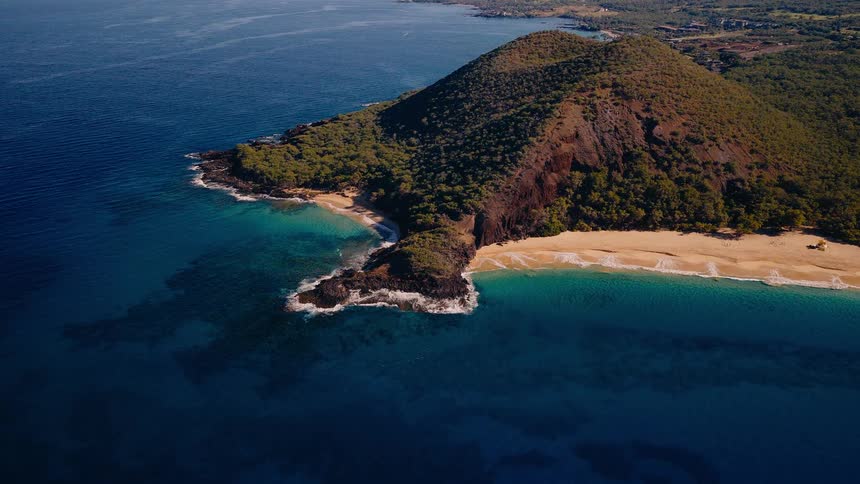A magnificent aerial view captures the beauty of a tropical island, featuring a lush volcanic cone, a golden sand beach, and the crystal-clear turquoise ocean